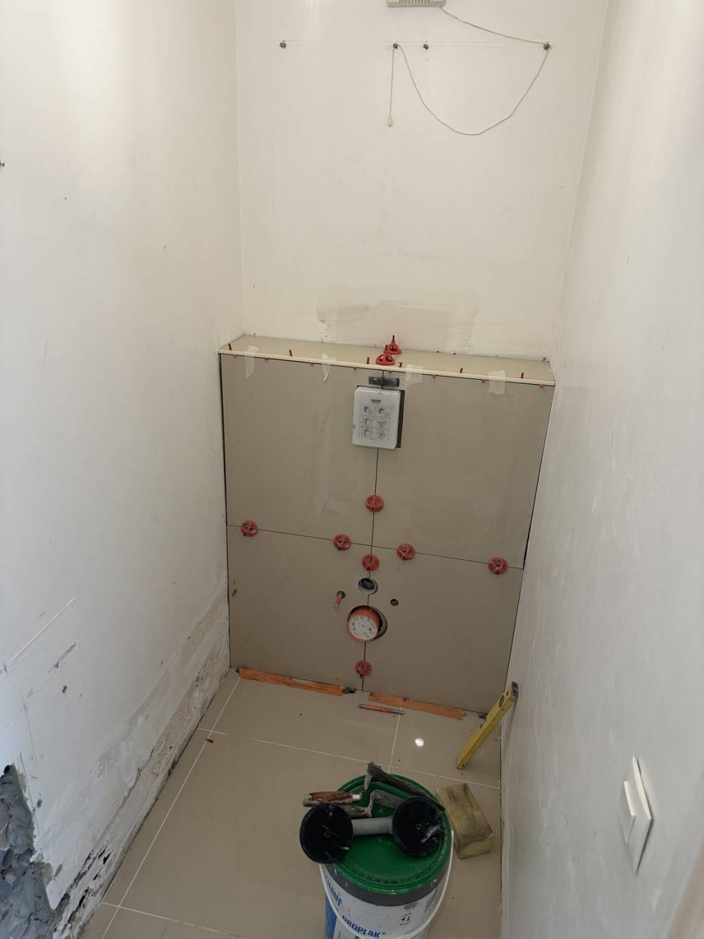Pose du carrelage sur coffrage wc suspendu avec système de nivellement pour garantir une surface régulière.